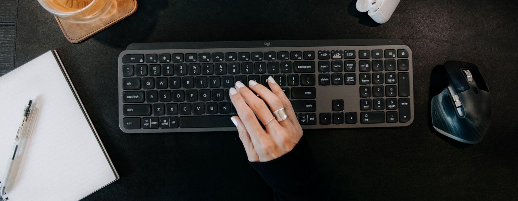 woman's hand on a keyboard surrounded by office items and a cup of tea on a coaster